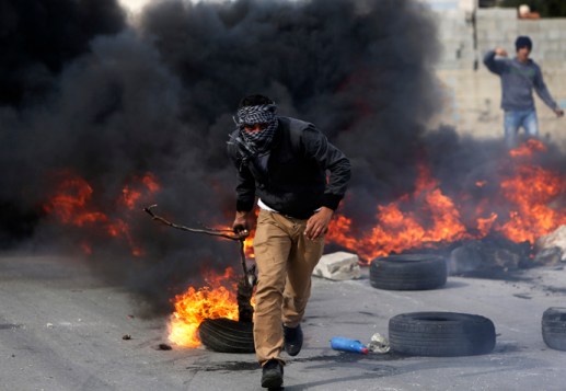 A Palestinian protester uses a branch to move a burning tyre during clashes with Israeli soldiers near&nbsp;Ramallah