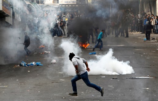 A stone-throwing Palestinian protester runs past tear gas fired by Israeli soldiers during clashes in&nbsp;Hebron