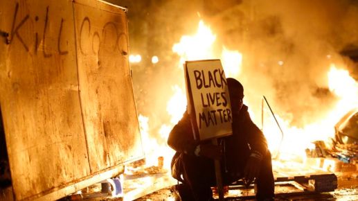 Demonstrator sits in front of a street fire during a demonstration following the grand jury decision in the Ferguson, Missouri shooting of Michael Brown, in Oakland,&nbsp;California